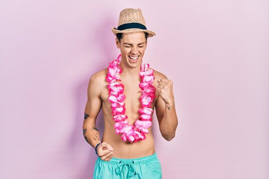 Young hispanic man wearing swimwear and summer hat celebrating surprised and amazed for success with arms raised and eyes closed
