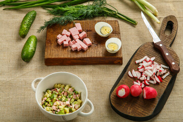 Okroshka in a tureen on the table on a tablecloth next to vegetables on boards.