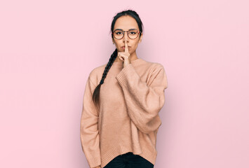 Young hispanic girl wearing casual clothes and glasses asking to be quiet with finger on lips....
