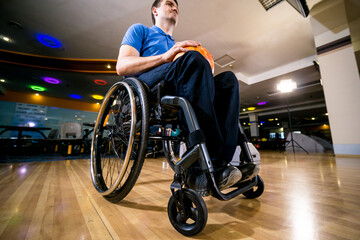 Young disabled man in wheelchair playing bowling in the club