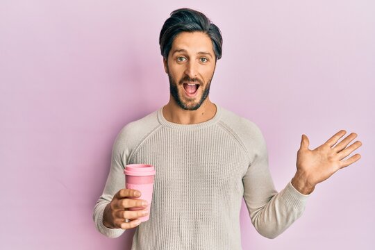 Young hispanic man drinking a take away cup of coffee celebrating achievement with happy smile and winner expression with raised hand
