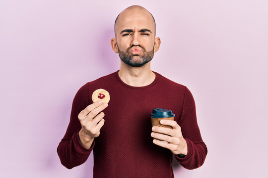 Young bald man drinking coffee and eating pastry looking at the camera blowing a kiss being lovely and sexy. love expression.