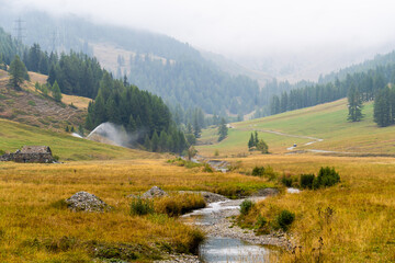 Veduta autunnale di un fiume che scorre in mezzo ai prati gialli a settembre in valle d'Aosta a...