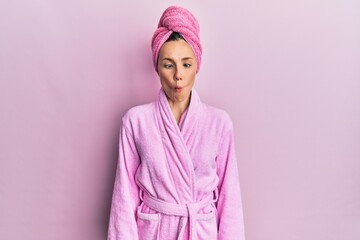 Fototapeta premium Young blonde woman wearing shower towel cap and bathrobe making fish face with lips, crazy and comical gesture. funny expression.