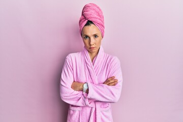 Young blonde woman wearing shower towel cap and bathrobe skeptic and nervous, disapproving expression on face with crossed arms. negative person.