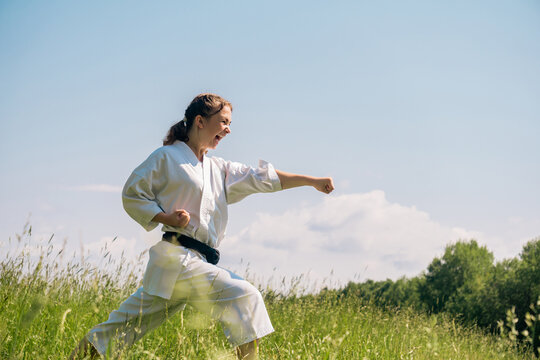 teen girl training karate kata outdoors, performing a strike oi zuki using kiai