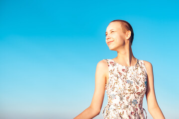 girl teenager in a dress with a short haircut looking into the distance, squinting at the sun,...