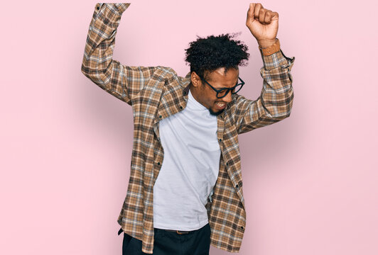 Young african american man with beard wearing casual clothes and glasses dancing happy and cheerful, smiling moving casual and confident listening to music