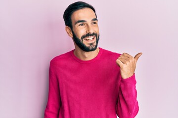 Fototapeta premium Young hispanic man wearing casual clothes pointing thumb up to the side smiling happy with open mouth