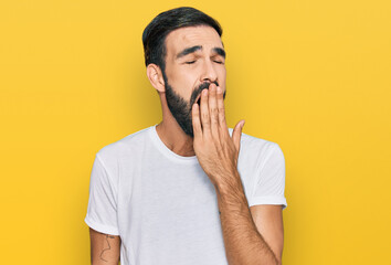 Young hispanic man wearing casual white t shirt bored yawning tired covering mouth with hand. restless and sleepiness.