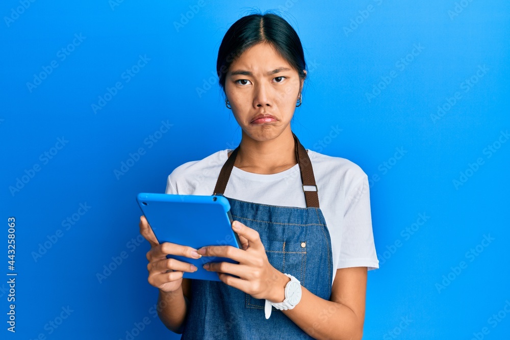 Sticker young chinese woman wearing cook apron using touchpad depressed and worry for distress, crying angry