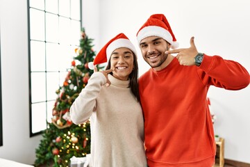 Young hispanic couple standing by christmas tree smiling cheerful showing and pointing with fingers...