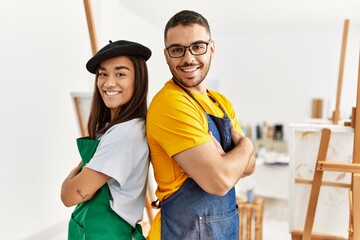 Young hispanic couple smiling happy standing with arms crossed gesture at art studio.