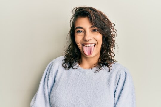 Young hispanic woman wearing casual winter sweater sticking tongue out happy with funny expression. emotion concept.