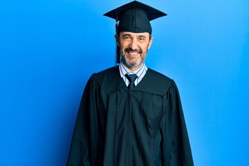 Middle age hispanic man wearing graduation cap and ceremony robe with a happy and cool smile on...