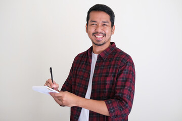 Adult Asian man smiling while writing on a note book