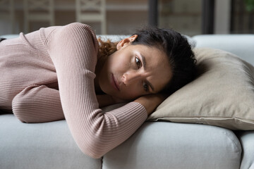 Unhappy hispanic latin caucasian woman lying on sofa, suffering from negative thoughts, getting...