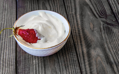 Natural homemade products, fresh strawberries in a cup with sour cream on a wood texture background, copy space. Natural organic yogurt on a brown rustic wooden table. Ecological products concept