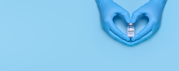 Doctor's hands in protective medical gloves hold a bottle of coronavirus vaccine in a heart-shaped gesture on a blue background. Vaccination. Immunization. Fighting the pandemic. Banner. Copy space - obrazy, fototapety, plakaty