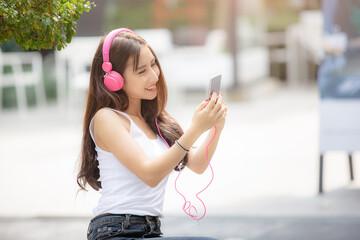 Happy young beautiful girl listening to the music with her pink headphones in the urban park