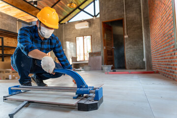 Select focus floor tile cutting equipment, Asian artisan tiler at construction site, worker cuts a...