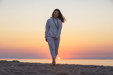 Fototapeta premium young smiling woman walking by sea beach on sunrise