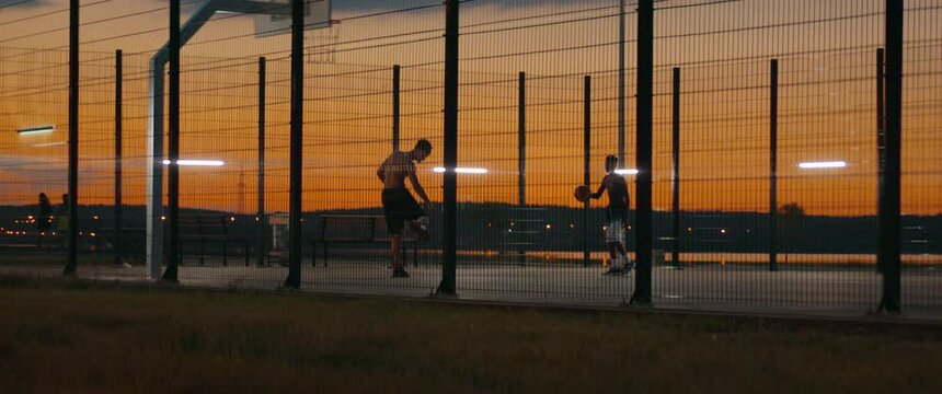 Two Black African American siblings or friends playing basketball on outdoor court in the evening. High quality 4k footage