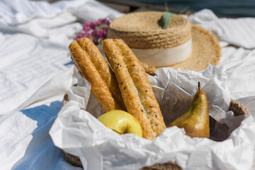 cozy picnic in nature, on the pier view from above. Fresh fruit, a basket of jute, a baguette, a white sheet. Two champagne glasses and a candle.