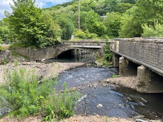 Fototapeta premium Small river, running alongside the, road, with trees and a bridge by, Burnley Road, Blackshaw, UK