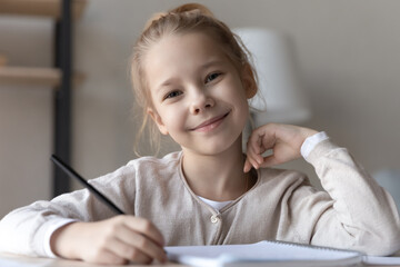 Happy schoolgirl. Headshot portrait of smiling small girl elementary school age pupil sit at desk...