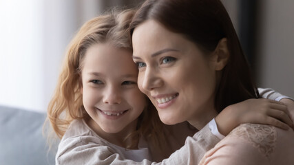 Feel safe in mother embraces. Happy little girl daughter cuddle up to affectionate single mom touch head look aside share most desired dreams. Young female parent imagine create plans with beloved kid