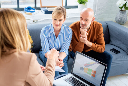 Couple Getting Advice From Businesswoman While Sitting At Home In The Living Room. Happy Couple Communicating With Their Financial Advisor While Sitting At Home On The Couch. 