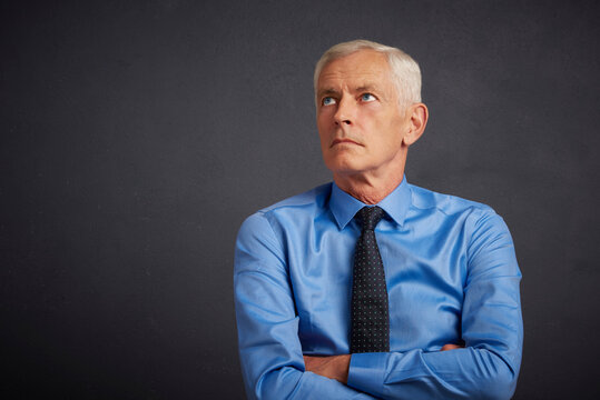 Cropped shot of handsome elderly man wearing shirt and tie while standing with folded arms at dark grey background. Senior man portrait.