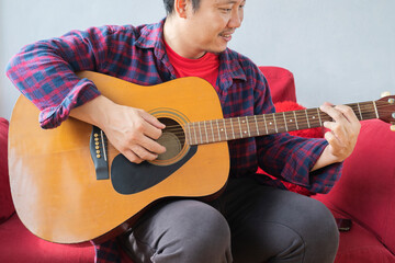 A 40 year old Asian man is practicing guitar.