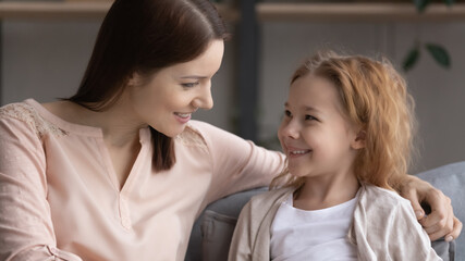 Pleasant conversation. Happy preteen girl sit on couch glad to talk to friendly female teacher psychologist answer questions discuss school life. Smiling little daughter ask supportive mom for advice