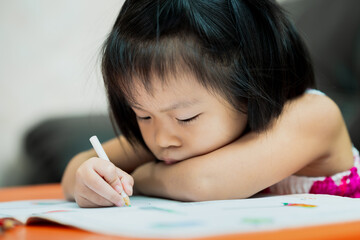 Cute Asian girl coloring in her homework book with wooden paints. Children are tired of doing a lot...