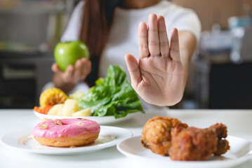 Woman on dieting for good health concept. Close up female using hand push out her favourite donut and choose green apple and vegetables for good health.