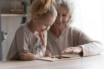 Indoor activity. Smiling elderly female babysitter engaged in logic game with little preteen girl...