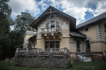 An old beautiful abandoned manor house in the forest. Blue sky with clouds. Green trees and grass. Ancient architecture of an abandoned building.
