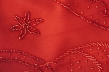Red fabric having seed bead floral design with decorative bungle beads and stitches.  Closeup of...
