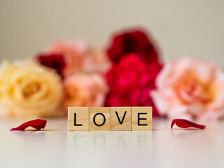 LOVE - napis z drewnianych kostek, róże w tle, różowy kolor © Klaudia Baran