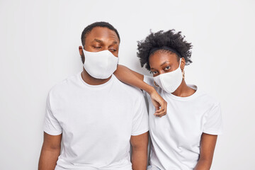 Serious dark skinned ethnic woman and man wear disposable protective masks against coronavirus stand closely to each other dont keep social distance dressed in casual white t shirt isolated.