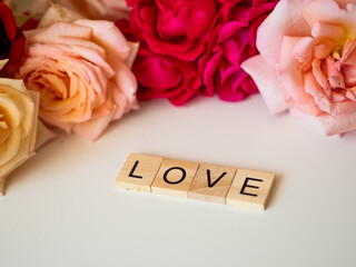 LOVE - napis z drewnianych kostek, róże w tle, różowy kolor © Klaudia Baran