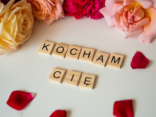 Kocham Cię - napis z drewnianych kostek, róże w tle, różowy kolor © Klaudia Baran