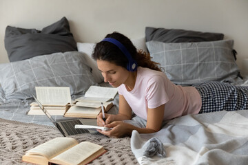 Smiling millennial hispanic woman in headphones lying on comfortable sofa, watching workshop course...