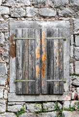 Window of old stone house is closed by wooden shutters. Close up.
