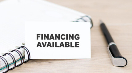 Financing Available text on card, next to a notebook and a pen on the table. Fundraising and additional support or donation. Business startup concept.