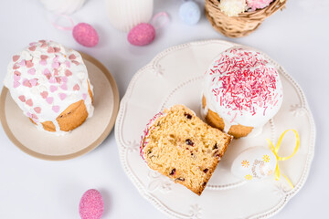 Fototapeta na wymiar Easter cake with raisins in sugar glaze. festive pastries with pink sprinkles, painted eggs, pussy willow and Easter decor on a white background. religious holiday 