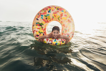 Joyful child on inflatable ring ride on breaking wave. Travel lifestyle, swimming activities....
