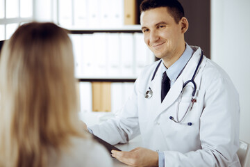 Friendly male doctor and patient woman discussing current health examination while sitting in sunny...